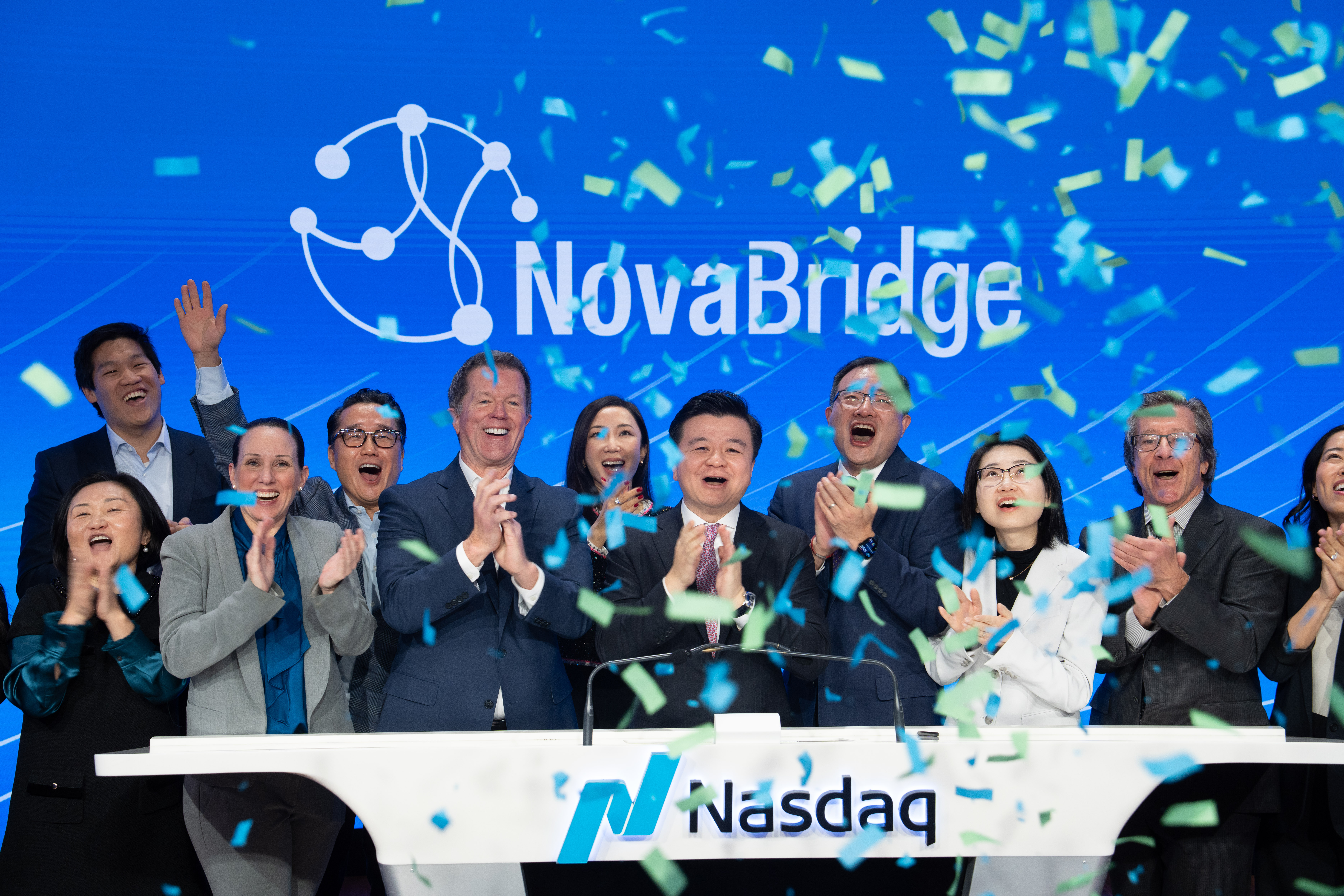 纳斯达克活动现场,人员在讲台后庆祝,彩带飘落,屏幕上显示 NovaBridge 标志。